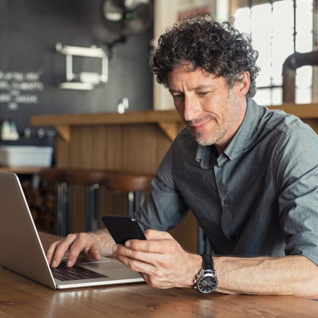 Person making a mobile payment or Interac e-Transfer from his smartphone while doing business on a laptop